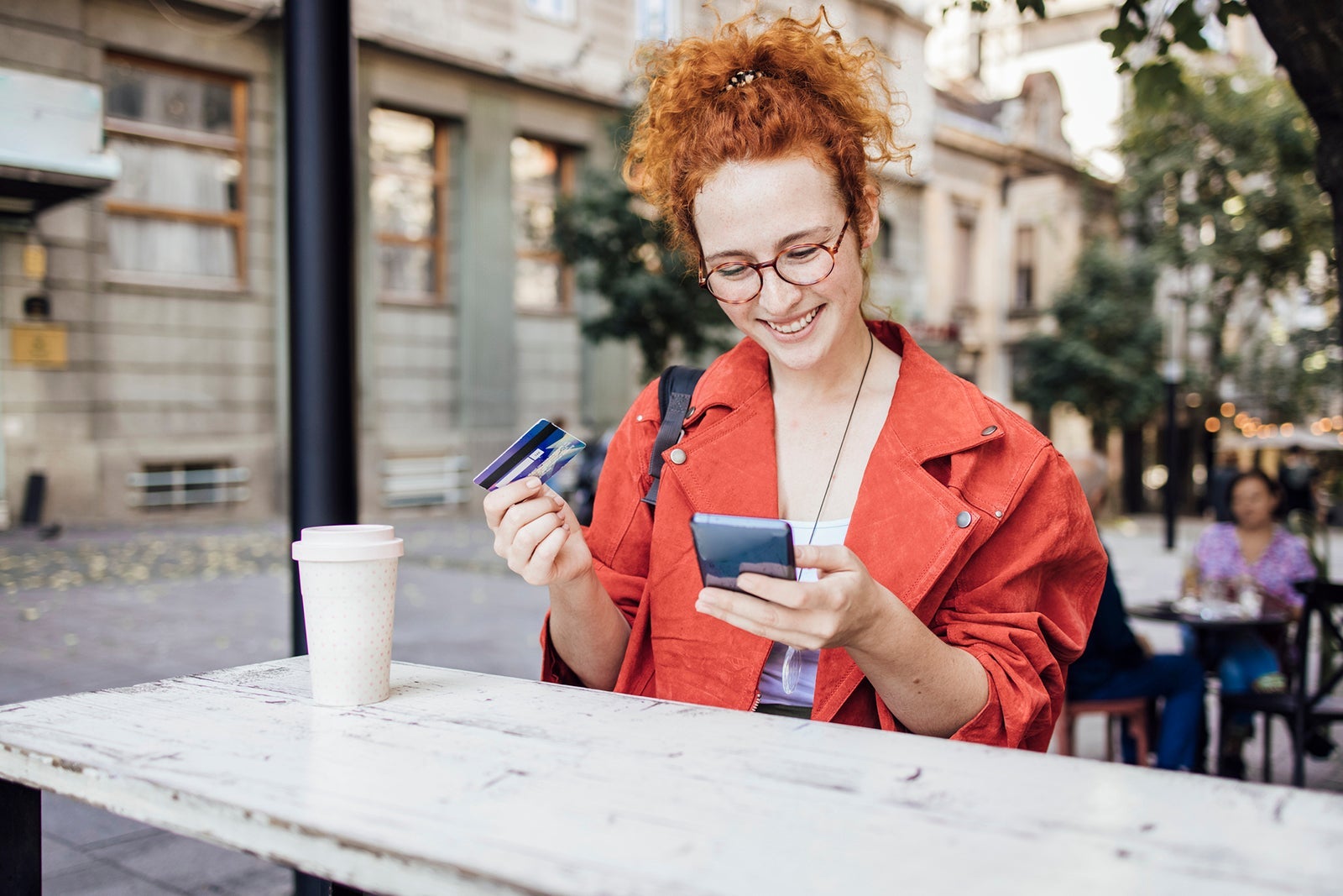 Portrait of a happy redhead girl enjoying coffee and shopping online at the cafe